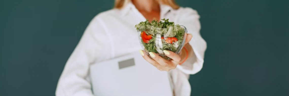 A woman with a vibrant smile offering a fresh salad bowl, promoting healthy eating.