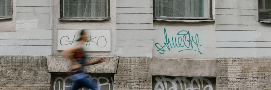 Blurred motion of a woman running past a graffiti-covered urban wall. Captures dynamic energy.